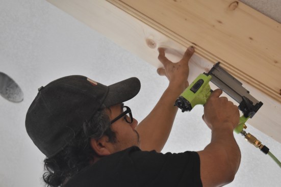 Using a 23ga nailer the worker installs the corner detail along the edges of the beams. 
