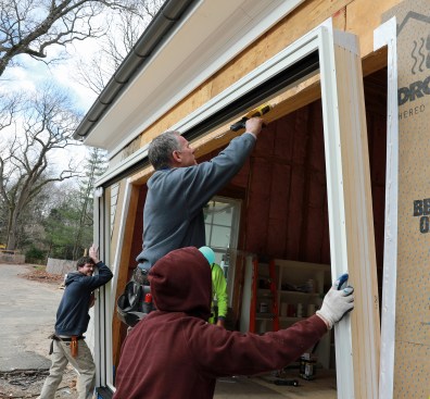 The crew tips out the frame so the flange can be caulked. Even though the flange will be flashed with a peel-and-stick flashing later, caulk is still required by the door maker.