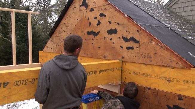 The carpenters set the end of the beam onto the temporary shelf, before securing it to the beam already embedded into the wall of the existing house.