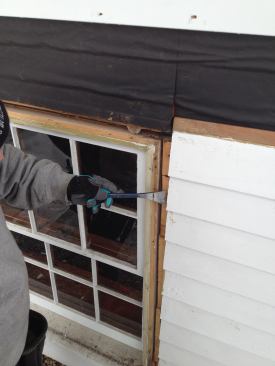 A pry bar slipped behind the clapboards along both sides of the window pulls them slightly away from the walls. This will let the flashing tape tuck behind without removal of the siding.