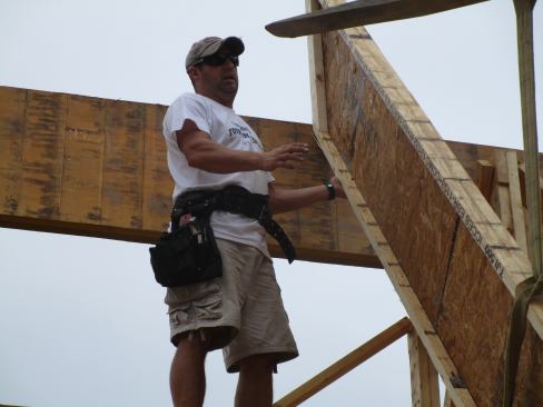 A framer catches the end of a wood I-joist common rafter, which will be attached to the face of the LVL ridge with structural fasteners. The rafters in this section of the roof are supported by the ridge beam as well as by the floor framing at the lower end.