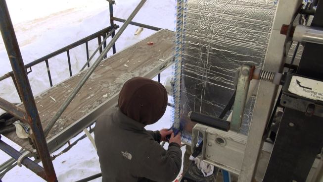 A worker applies Dow Weathermate tape to the inner layer of rigid foil-faced foam.