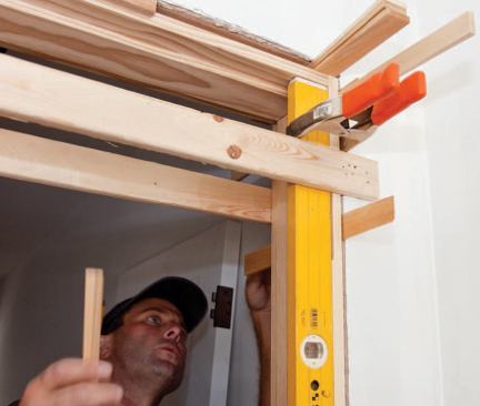 A door-length level clamped to the jamb provides a reference for both plumb and straight, leaving hands free to insert and adjust the shims.