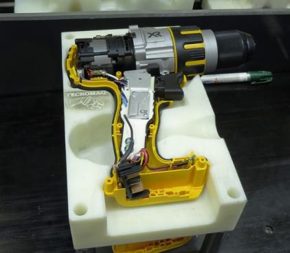 The switch, motor, and gear/chuck assembly have been placed in a “clamshell” housing that is resting in an assembly jig. The next step is to place the other half of the housing over this one and screw it in place