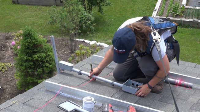 On the roof, electrician apprentice Mel Janarelli assembles a run of PVC conduit that will hold the grounding cable and direct-current conductors from two “strings” of photovoltaic modules (nine panels per string, for a total rated output of roughly 4,000 watts).