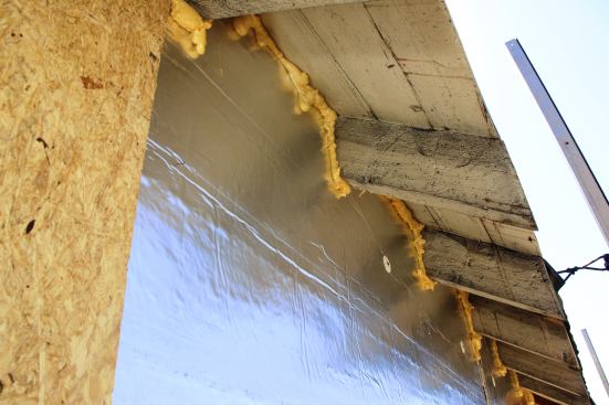 The airtightness problem at the top of the existing wall posed a complicated puzzle. Remodeler Heather Thompson says the team contemplated cutting the rafters off flush with the outside wall and continuing the airtight membrane up the wall and onto the roof sheathing, but elected instead to leave the existing rafters in place in order to avoid the complicated labor of completely rebuilding the eaves. So instead, the crew had to cut foam insulation to fit around each rafter, sealing the joints with can foam as shown here.