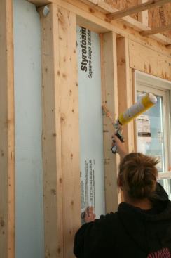 Required to put in hundreds of hours of labor, the soon-to-be owner pitches in to seal the foam insulation in the stud bays.