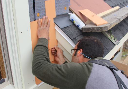 Pollard checks the fit of a scribed cut. The shingles are spaced off the roof head flashing and roofing by 1 inch to provide an air inlet and to keep the wood siding away from roof runoff.