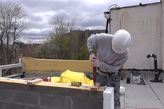 A powder-actuated fastener is used to drive hardened masonry nails to attach a wood nailer to the concrete cap of a masonry parapet wall.