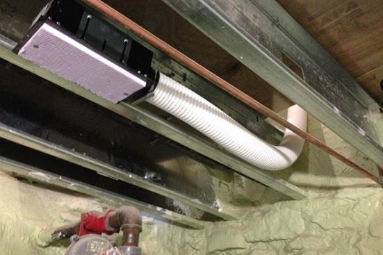 Corrugated plastic tubing for the energy recovery ventilator terminates in a ceiling register in the basement level of the house, covered for temporary protection with pink insulation foam. Ventilation airflows for the home are too slow and low-volume to supply heating or cooling air, or to create significant mixing of air. The larger ductwork of the mini-split heating and cooling system, with its more powerful air handler, provides those functions, while the heat recovery ventilator supplies tempered fresh air to each room and pulls humidity and odors out of the house through return grilles located in the bathrooms and kitchen.