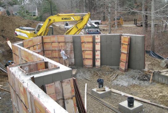 Slab areas were poured atop full-height foundation compartments. The smaller of the two compartments is visible on the left side of the photo; the larger, not yet complete, is defined by the row of vertical rebar visible at the rear.