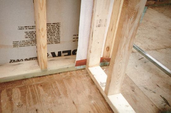 Where a partition intersects an exterior wall, a strip of poly is installed on top of the 2x8 drywall nailer before the partition is built. Note that the wall poly is taped to the Tenoarm poly that protrudes from under the bottom plate.