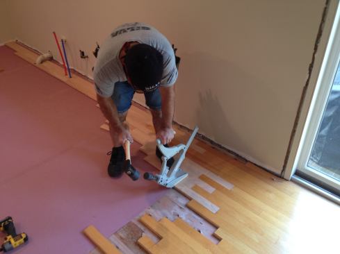After driving the board into place, Manny uses a floor nailer to secure it. If too much of the board is left unattached face screws can be added.