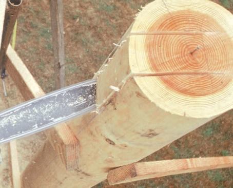 The carpenter makes the cutout with a chain saw, working off staging for stability.