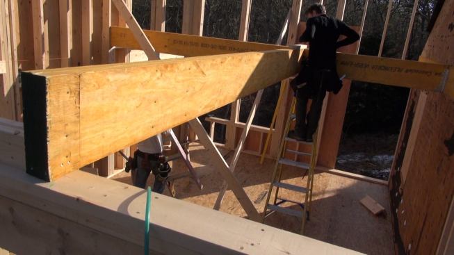 Laffin and Hill set the next beam for the floor system, which defines the stair opening. Where this beam meets the main beam, a temporary scab screwed into the top of the new beam holds the two beams flush at the top. The near end of the beam sits atop a double two-by-four buildup of the outside wall of the addition.