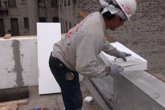 EPS foam is cut with a handsaw before fitting the foam into place on the top cap of a masonry parapet wall.