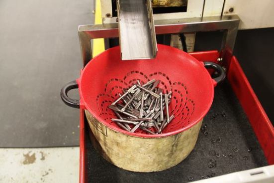These Phillips blades have just been machined in a CNC lathe. They came down the chute at the top of the photo and landed in a kitchen colander—which allows the oil used in the machining process to drain off the pieces.