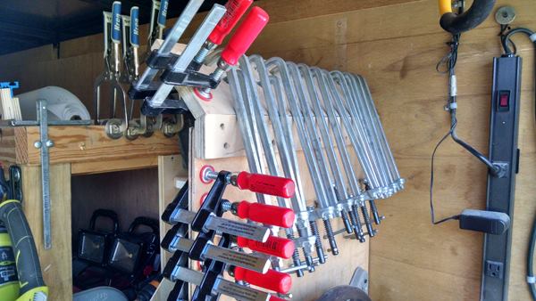 Clamps store at the back rear end of the trailer; F-clamps and Kreg clamps hold themselves in place. The all-metal clamps to the right hang from holes and are used with the dog holes in Gullion’s work station and the bench in the trailer.
