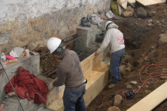 Workers assemble plywood forms in preparation for a concrete pour. The job was staged in order to maintain stability of the shared basement wall: end and center sections of the buttress were formed and placed first, then the center sections were excavated, formed, and poured.