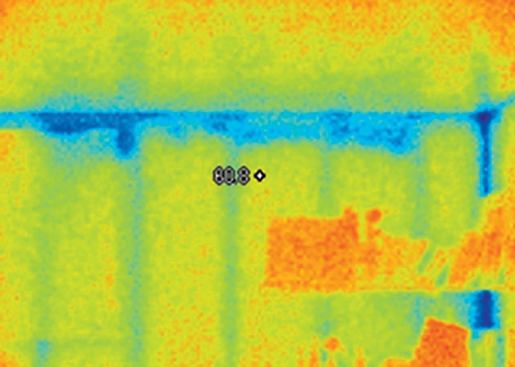 An image of the same wall taken under higher delta-t conditions (from a slightly different angle) reveals voids in the insulation below the top plate. A bookshelf and other furnishings are visible on the right-hand side of the image.