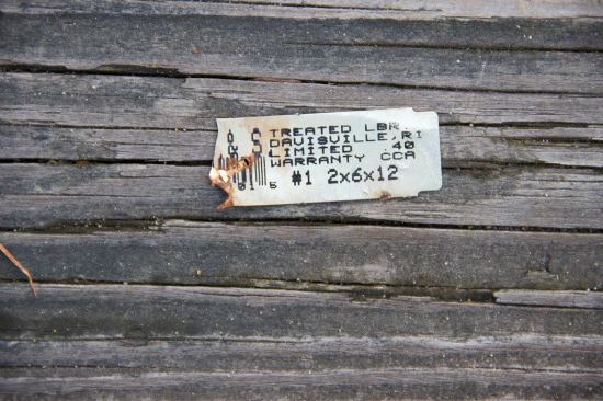 A closeup of the label still attached to the old CCA staircase built on ground in North Dartmouth, Mass., in the 1990s. The number “40” in the label refers to the treatment formula concentration, or “retention” — 40 pounds of retained copper per cubic foot, the level specified for fence posts, landscape ties, and poles in ground or fresh water. This label was taken from a 2x6 board on the walkway, indicating how all treated wood was customarily treated for ground contact in the late 20th century.