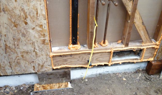 When wall sheathing is set in beads of polyurethane foam, temporary blocks at the base make it easier to position the sheet without smearing the sealant.