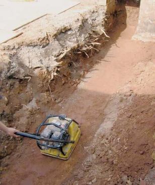 He uses a plate compactor to prepare the soil underneath the footing.