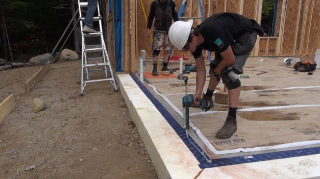 Air-sealing for the panelized version of this wall system relies more heavily on caulks and sealants than does the site-built version, where continuous membranes would be applied after the framing is complete. Here, a crew member applies sealant to the foundation slab where the wall plate will meet the slab.