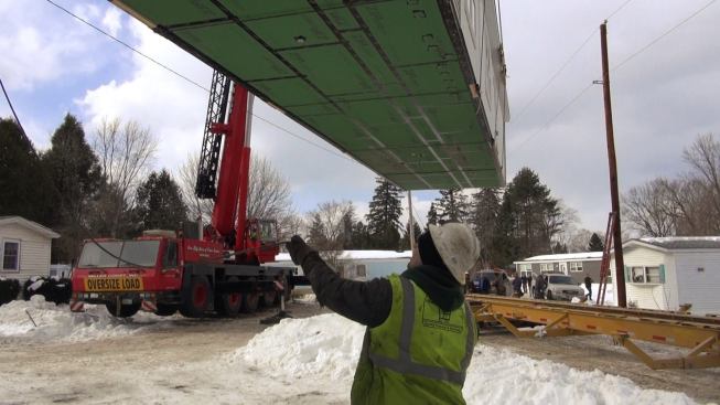 As a ground guide works the tag line, the crane lifts the heavy modular unit off the trailer. From this point of view you can see the taped ZIP Sheathing underside of the trailer, which forms part of the unit's air-tight high-performance envelope.