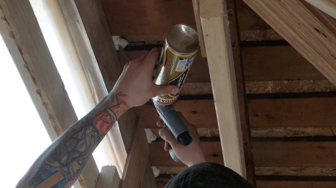 An insulating crew member squirts gun foam into gaps between the existing roof’s skip sheathing.