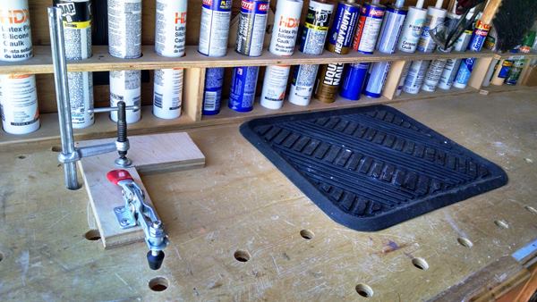 Caulk is difficult to find and keep track of when stored in a bucket or bin; Gullion keeps it out where he can see (and get at) it. Note the dog holes in the work bench. One is being used to clamp down a quick release clamping jig. The rubber floor matt to the right is used as a surface for mixing stain. If anything spills the raised edges of the matt keep it from spreading.