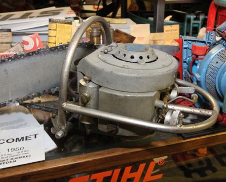 The gray machine is a diesel chainsaw built in Norway in 1950. The brand is Comet, which later became Jonsered. The designers thought a diesel chainsaw would be powerful and efficient. They were wrong. The saw was slow and complicated, and it quickly failed in the marketplace. 
Click here to see a shaky and smoky video of a Comet diesel chainsaw in action. If they were all that smoky then I can see why the product failed.