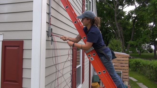 With the conduit run fully connected, the electrical crew continues snaking the wires that connect the rooftop solar array to the inverter. Here, Mel Janarelli feeds the conductors and ground wire into the conduit from outside the garage.