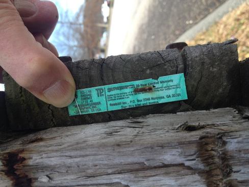A close-up of the label on a piece of CCA-treated wood on a guardrail by a road in North Dartmouth, Mass., near New Bedford south of Boston. The label specifies a chemical loading or “retention” of 40 pcf, suitable for ground contact, although the wood is installed above the ground. The wood has weathered, but is sound and free from rot, despite being subjected to years of damage from road salt, snowplowing, vehicle contact, and weed-whacking.