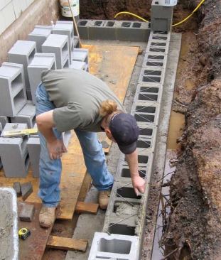 Blockwork starts at the corners, with the blocks laid in a full bed of mortar. Strings stretched between the corner blocks keep the courses straight. Every other course is reinforced with galvanized metal truss.