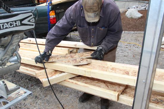 A carpenter sets up a jig to mark and cut the top ends of the wood I-joists for the wall at an angle matching the roof slope.