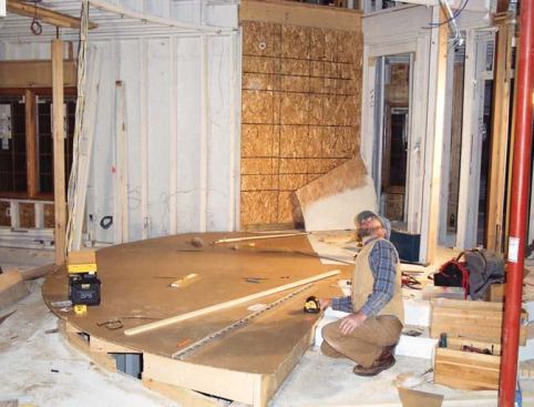 The author begins the new set of stairs by building a temporary platform over the basement stair opening and transferring key locations onto a hardboard template. Here he uses a laser to plumb down the location of the balcony header.