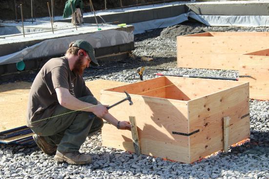 Carpenter Matt drives a stake into the trap rock sub-base to secure a plywood pad footing form in position.