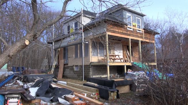 This perspective view of the house early in the project shows several aspects of the planned comprehensive makeover. The unreinforced block foundation at bottom will be undermined and supported from below with a new poured concrete footing, then insulated and frost-protected with below-grade wing insulation. The newly framed and sheathed corner was previously part of the wrap-around open porch, but will now become enclosed and conditioned living space. The complex framing of the second-story roof and dormers has been pulled back into shape after years of sagging and slumping, and will be deepened, reinforced, and heavily insulated. Another dormer will be added at the back of the house, and skylights will be included in the roof plane shown here.