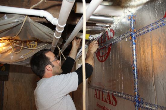 Mark Pollard insulates and seals the gap at the top of the basement wall with a can of gun foam.