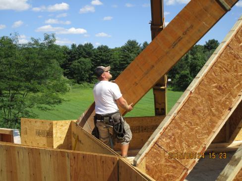A framer guides an LVL hip member into place in the roof frame. Obviously, the carpenter is not physically carrying the massive wood member — the forklift is supporting the weight of the manufactured timber.