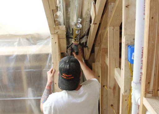 An “Itchy and Scratchy” worker uses gun foam to seal and insulate small gaps in the wall and rafter framing.