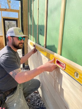 Every few courses, a carpenter checks that the siding is level. 