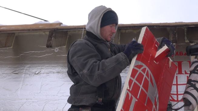 Carpenter Chris Mitchell cuts a notch in a sheet of foil-faced polyiso foam in order to fit the foam neatly around a roof rafter tail. Thompson Johnson has opted to fit the insulation and air seal around the existing rafter tails for this job, rather than cut the tails off and run the air barrier continuously up the walls onto the roof.