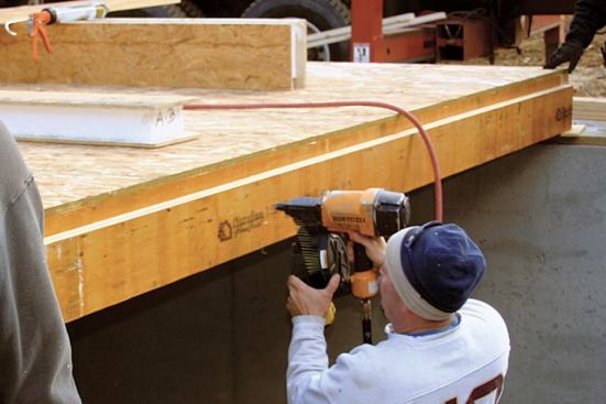 In preparation for the SIP floor for this 8-by-16-foot sunroom addition, the crew fastens an LVL ledger beam to the edge of the conventionally framed main floor, leaving a shimmed space below the ledger to receive the bottom edge of the panel.