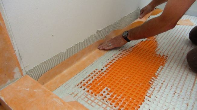 Boucher gently presses the strip of Kerdi membrane into the prepared mortar bed at the wall joint.