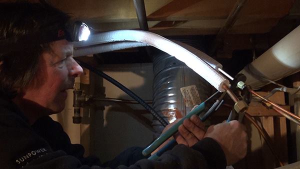 Working in the home’s basement with a headlamp for light, Chris Blaisdell connects a refrigerant line for the indoor fan unit.