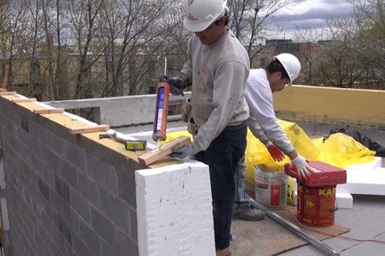 Adhesive caulk is applied to the face of a 2x4 nailer before attaching it to the poured concrete cap of the masonry parapet wall.