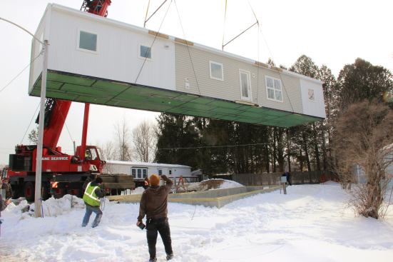 Crew members pass signals and haul tag lines as the crane cautiously maneuvers the unit around ground obstructions.