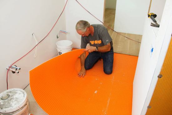Boucher lays the Ditra decoupling membrane onto the wet mortar. The mortar will work its way into the keyed polyethylene sheet, and also lock into the fleece underside of the material for a mechanical bond. In service, the Ditra's pliability and flexibility will prevent normal expansion or contraction of the subflooring from applying excessive stress to the relatively brittle tile and grout.
